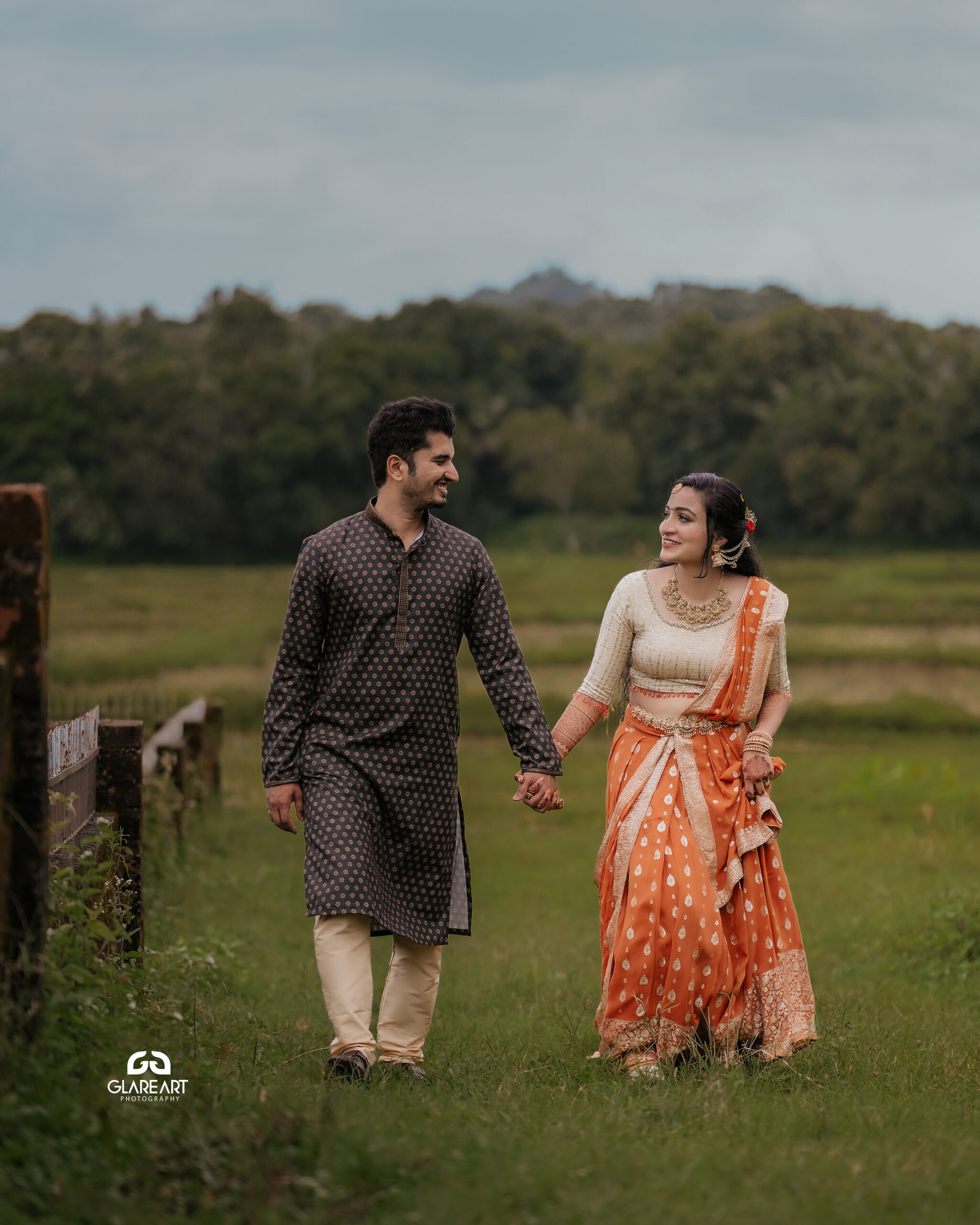 This is a lovely engagement-style photograph set in a natural outdoor location. The scene captures joyful and candid moments, emphasizing cultural attire- best wedding photography in Palakkad-wedding photography Palakkad
